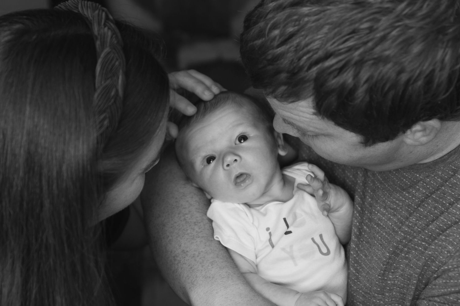 Black and white photo captures parents admiring their alert baby.