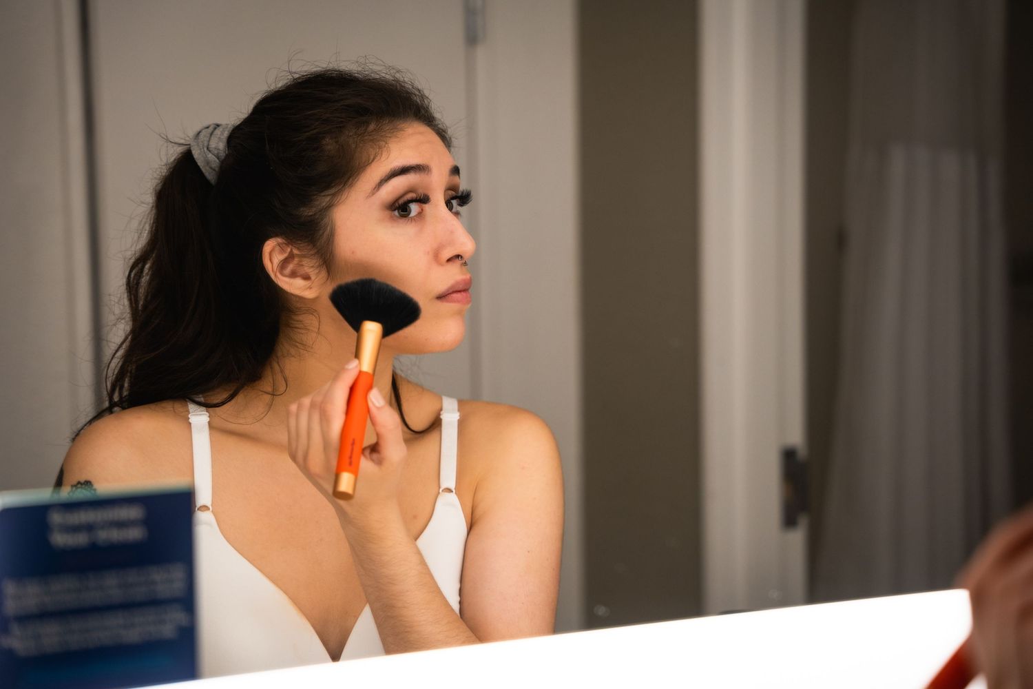 A person applying makeup with a brush while looking in a mirror.