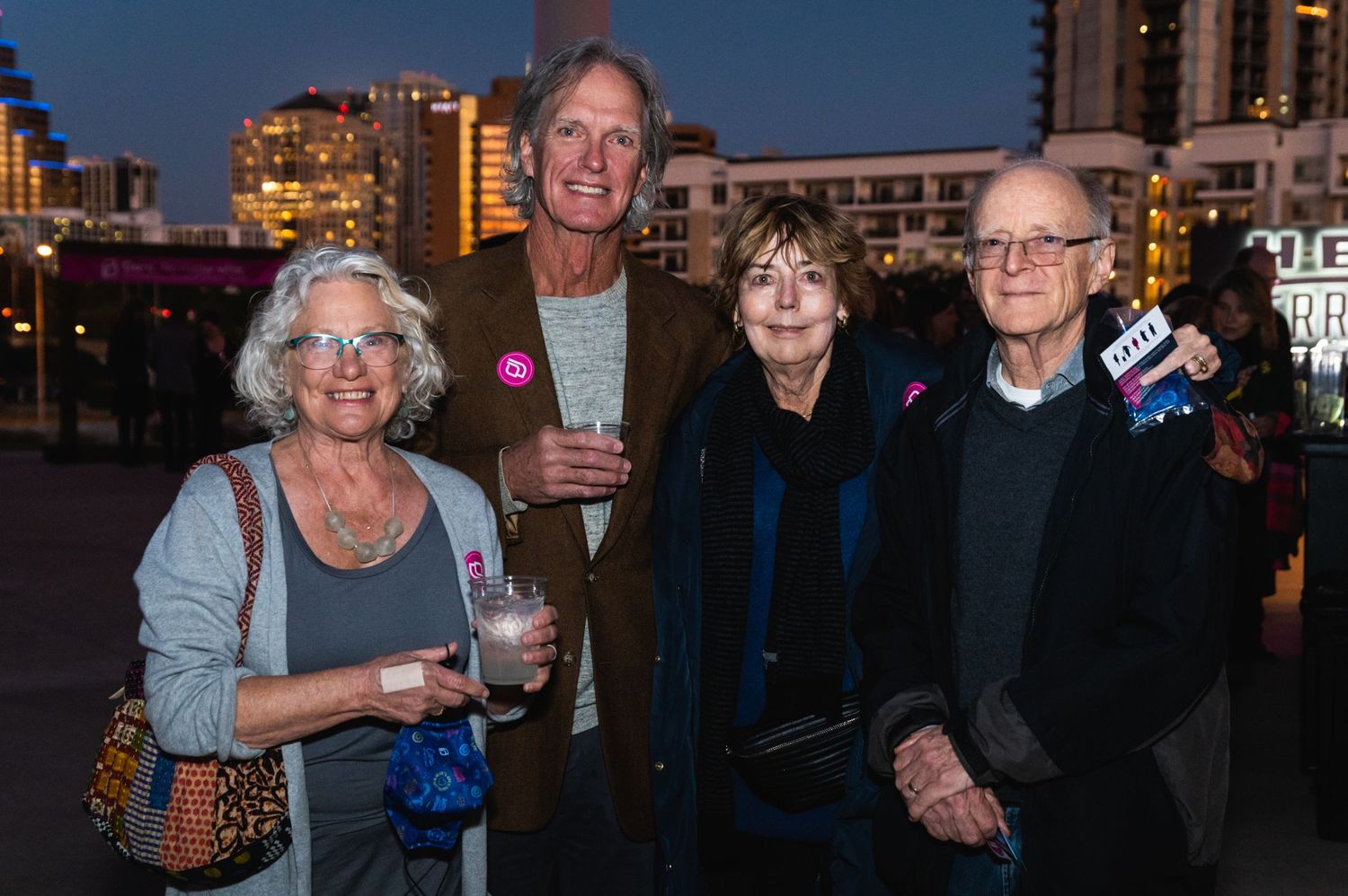 Group of people gathered at evening event with city lights in background.