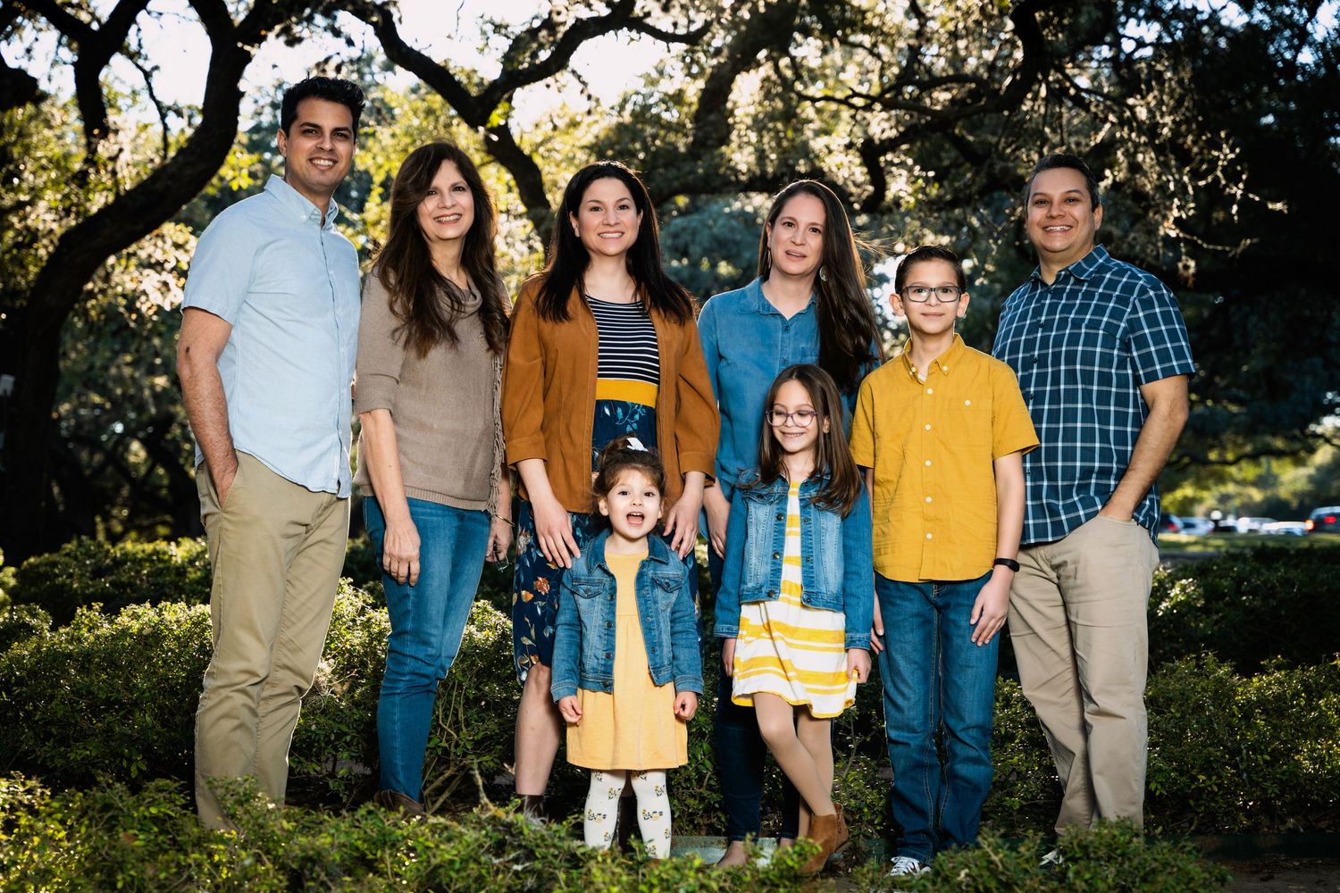 Multi-generational family portrait taken outdoors among oak trees at sunset.