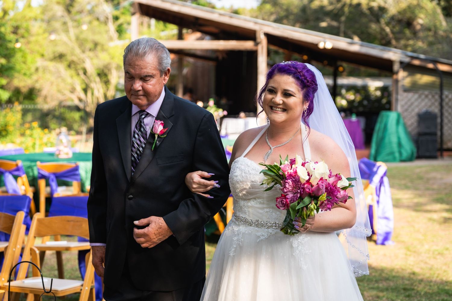 An outdoor wedding ceremony with colorful wooden chairs in the background.