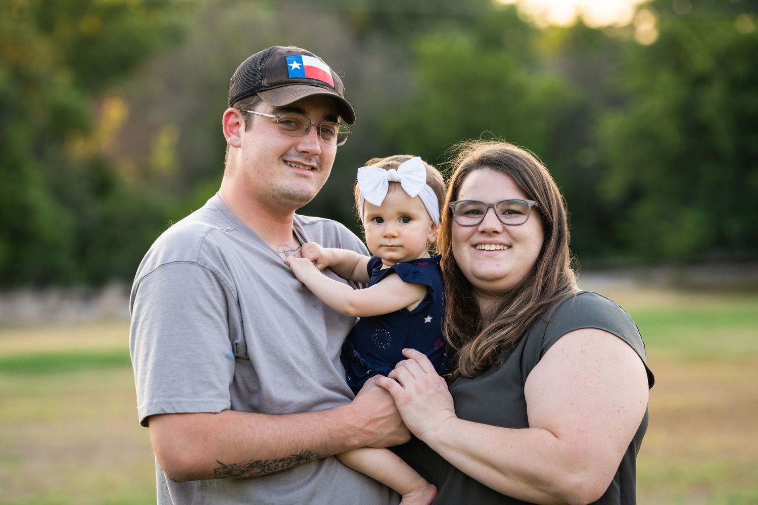 A family poses together at sunset in a grassy outdoor setting as they share a tender moment.