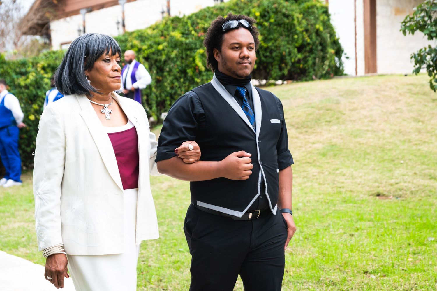 Two wedding guests in formal attire stand outdoors at a wedding ceremony venue.
