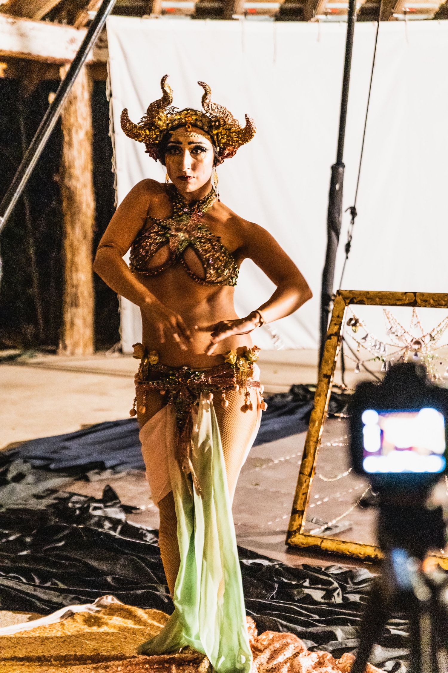 A performer wears an ornate horned headdress and fantasy costume on stage during a theatrical production.