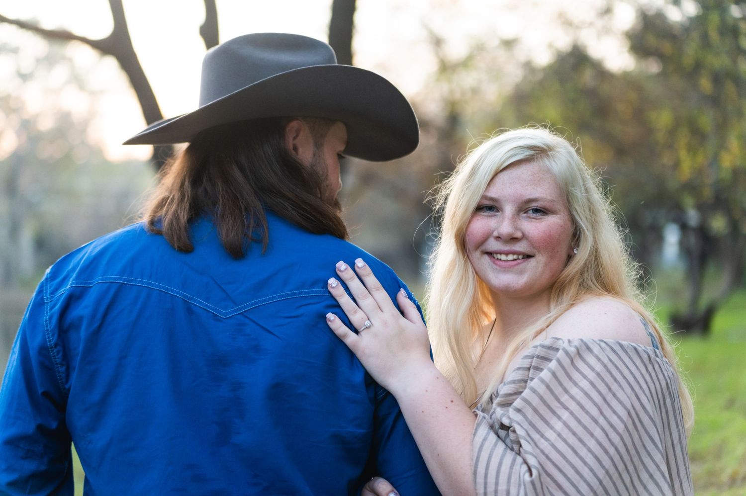 A couple shares a playful moment outdoors with her hand on his back.