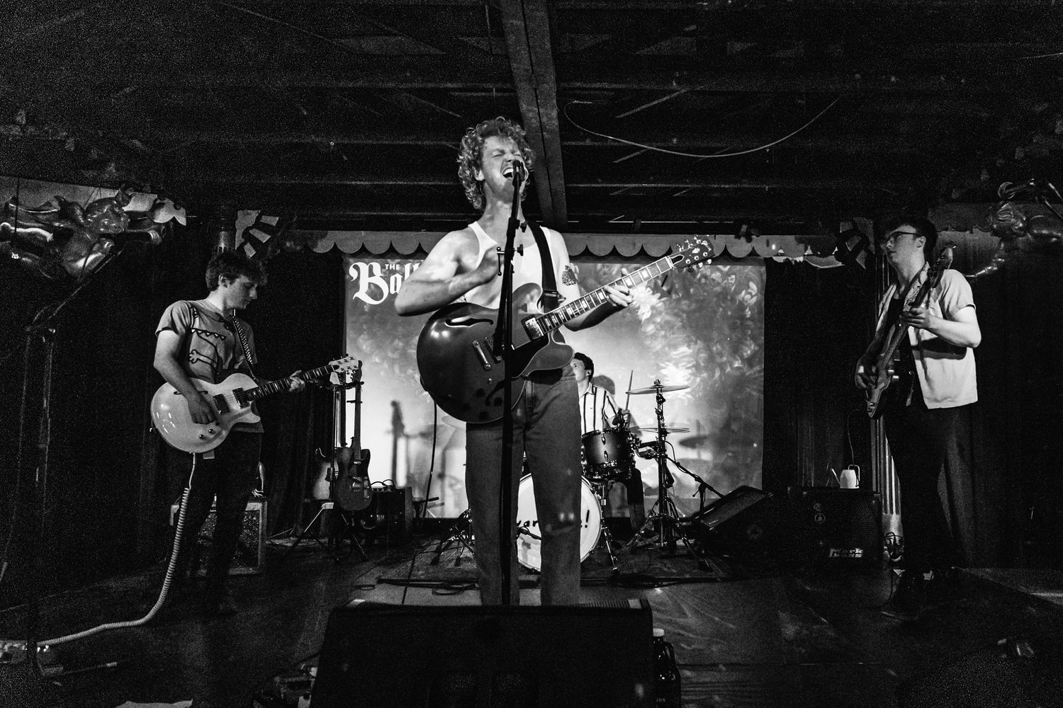 Band performs on dimly lit stage with dramatic lighting and projected backdrop.