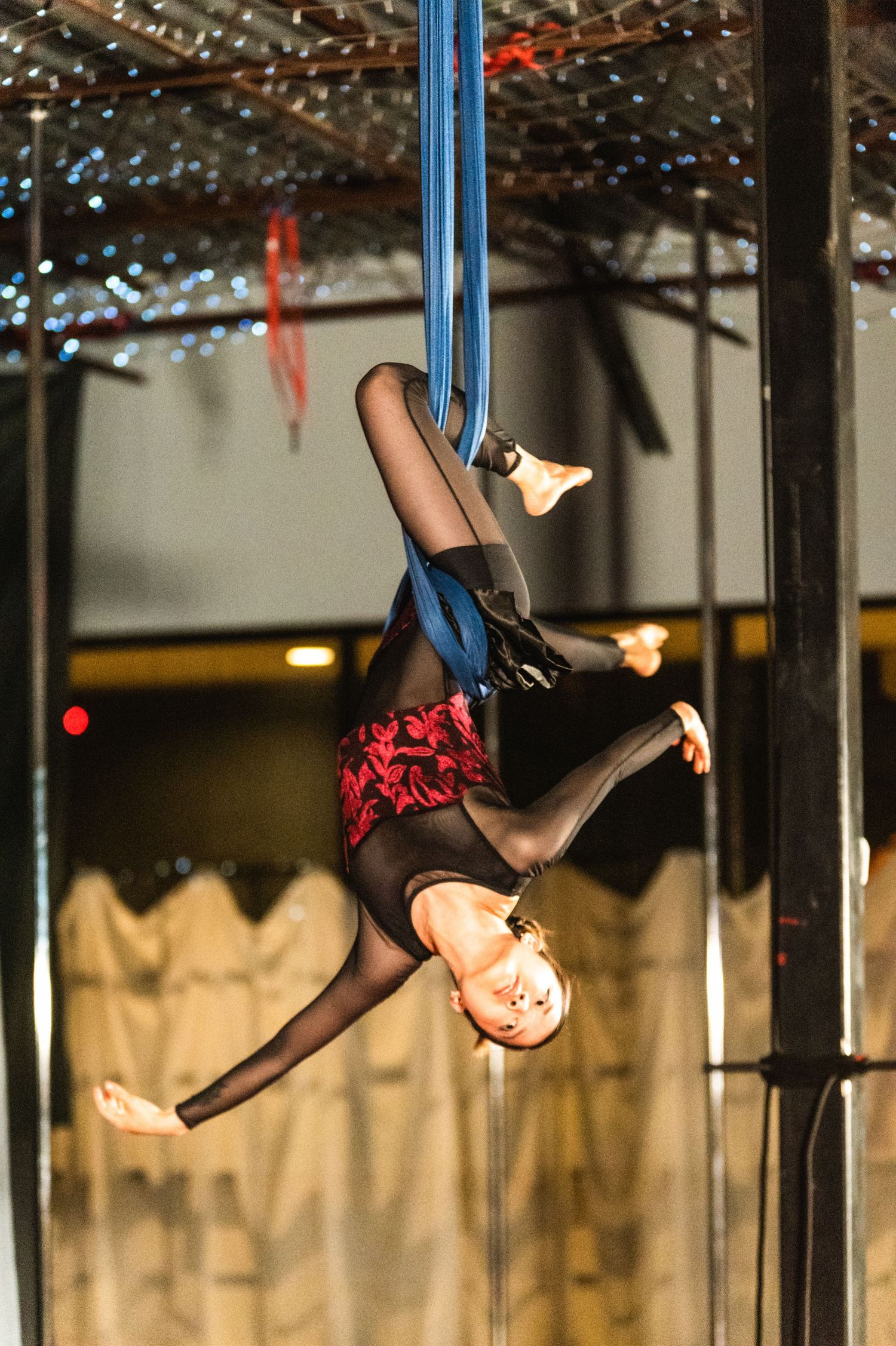 Aerial performer executes inverted pose on blue silks during theatrical performance.