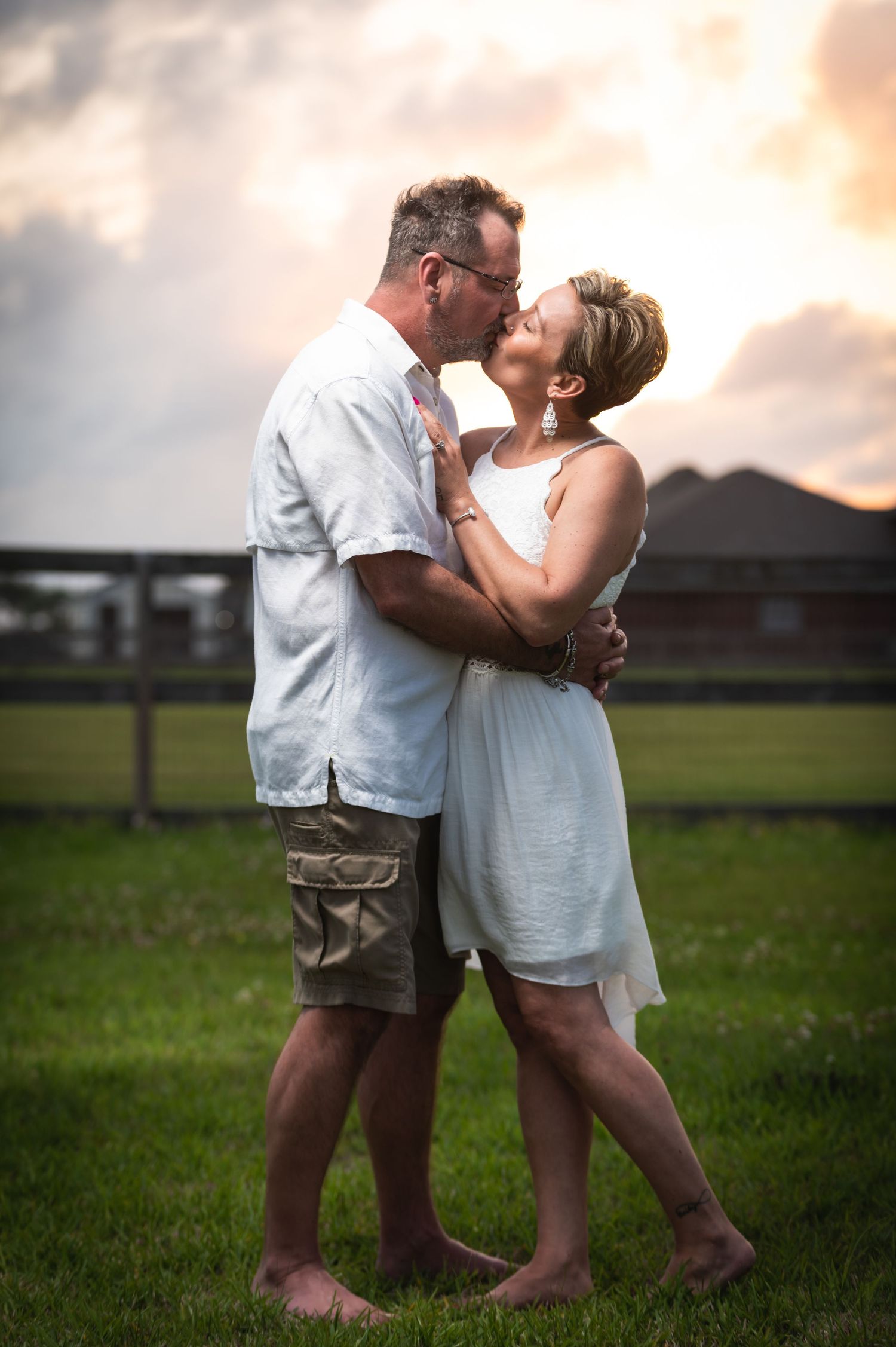 A couple embraces during golden hour in a backyard setting with houses in background.