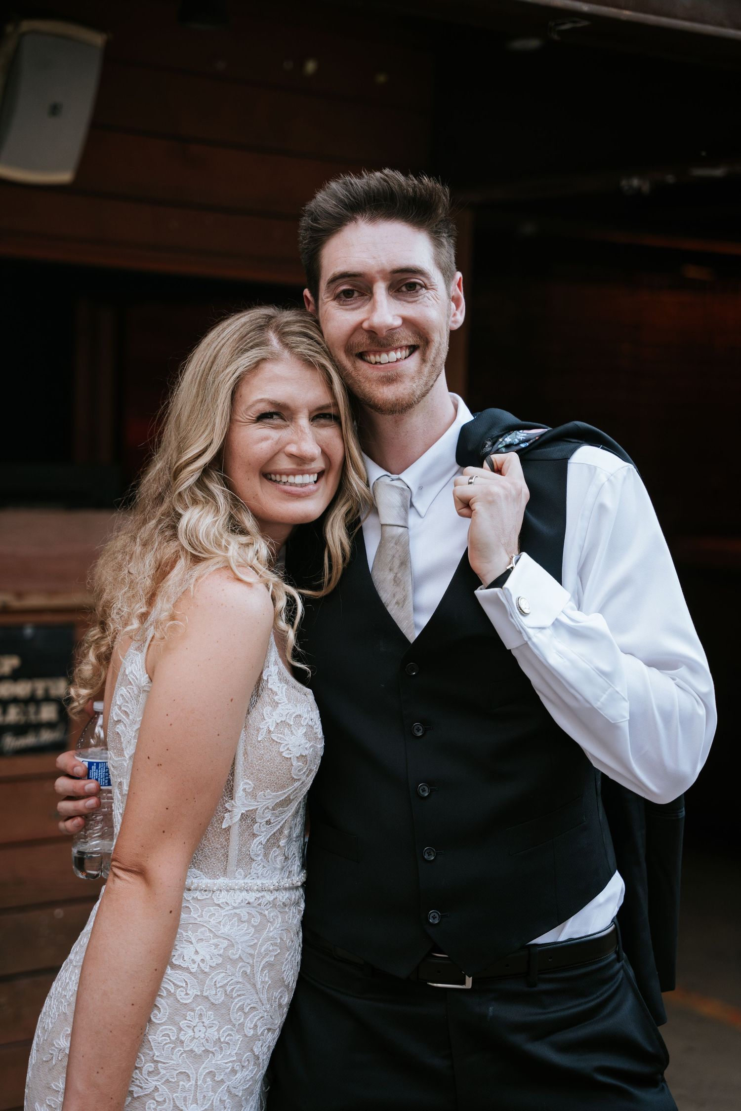 Newlyweds pose together at their wedding celebration, with the bride in a lace dress and groom in formal attire.