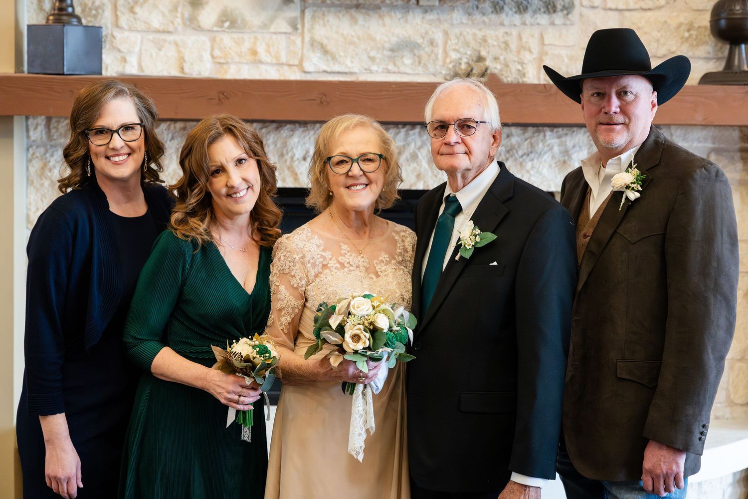 A group of five people dressed in formal attire stand together at a celebratory event in front of a stone fireplace.