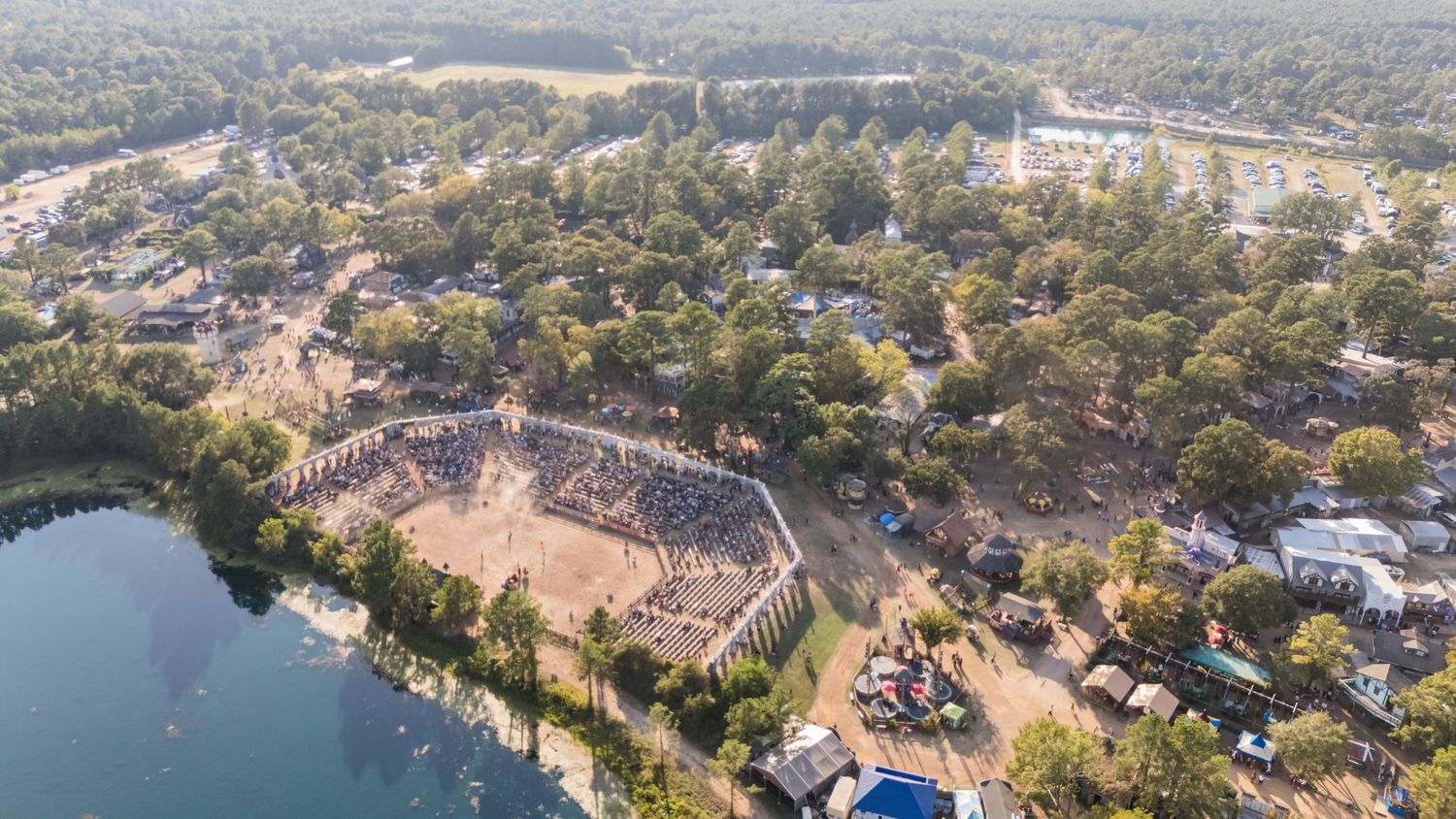 Aerial view of a Renaissance festival fairgrounds with buildings and amphitheater next to a lake.