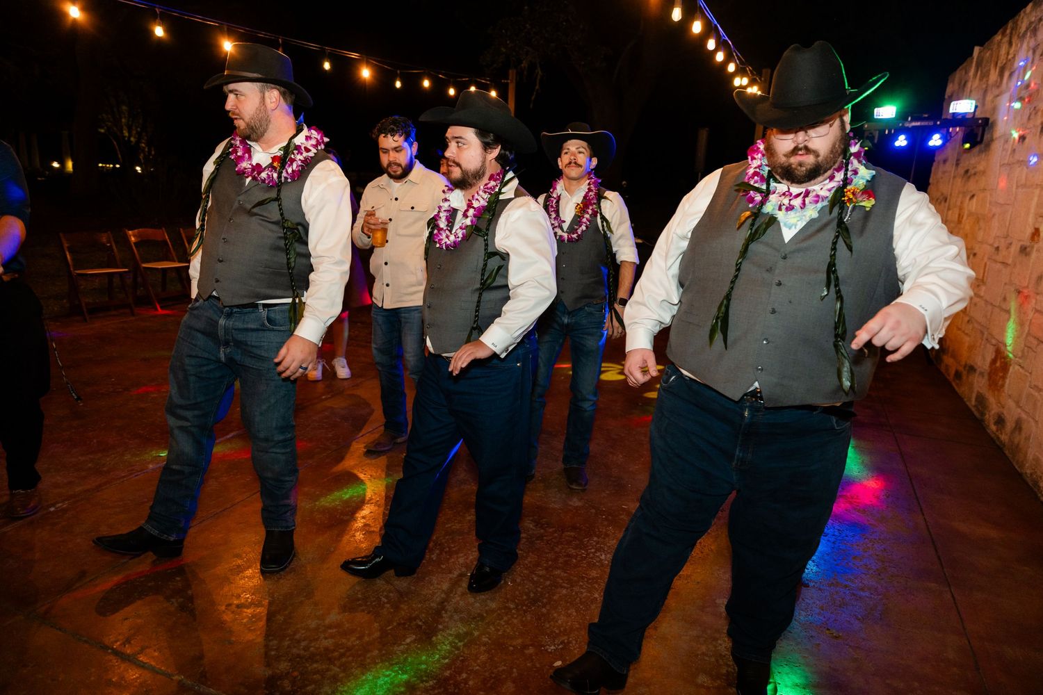 Line dancers in western attire performing choreographed moves under colorful party lights.