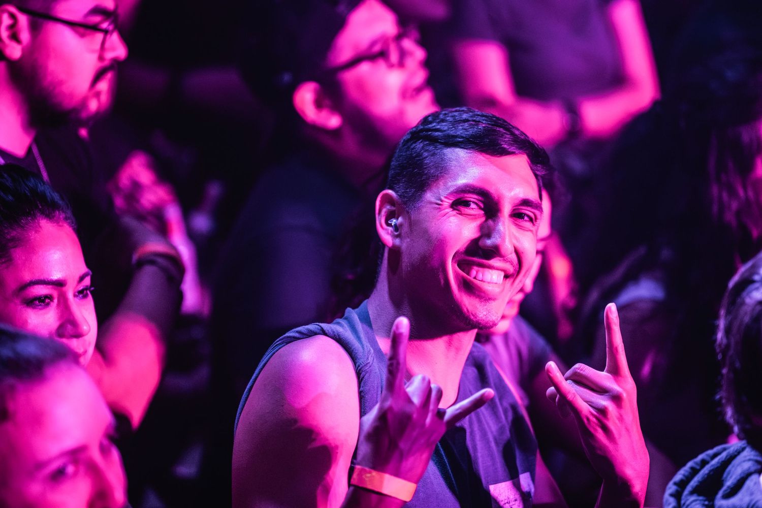 Concert audience member enjoying live music performance under purple lighting makes rock hand gesture.