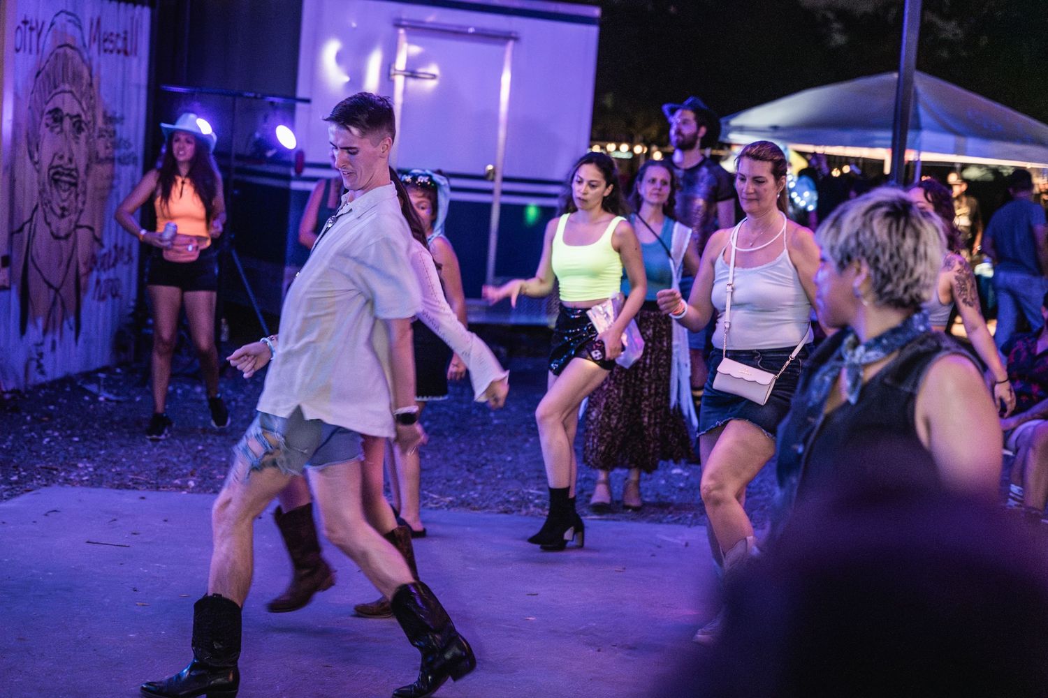 Dancers move energetically at an outdoor nighttime event illuminated by purple lighting.