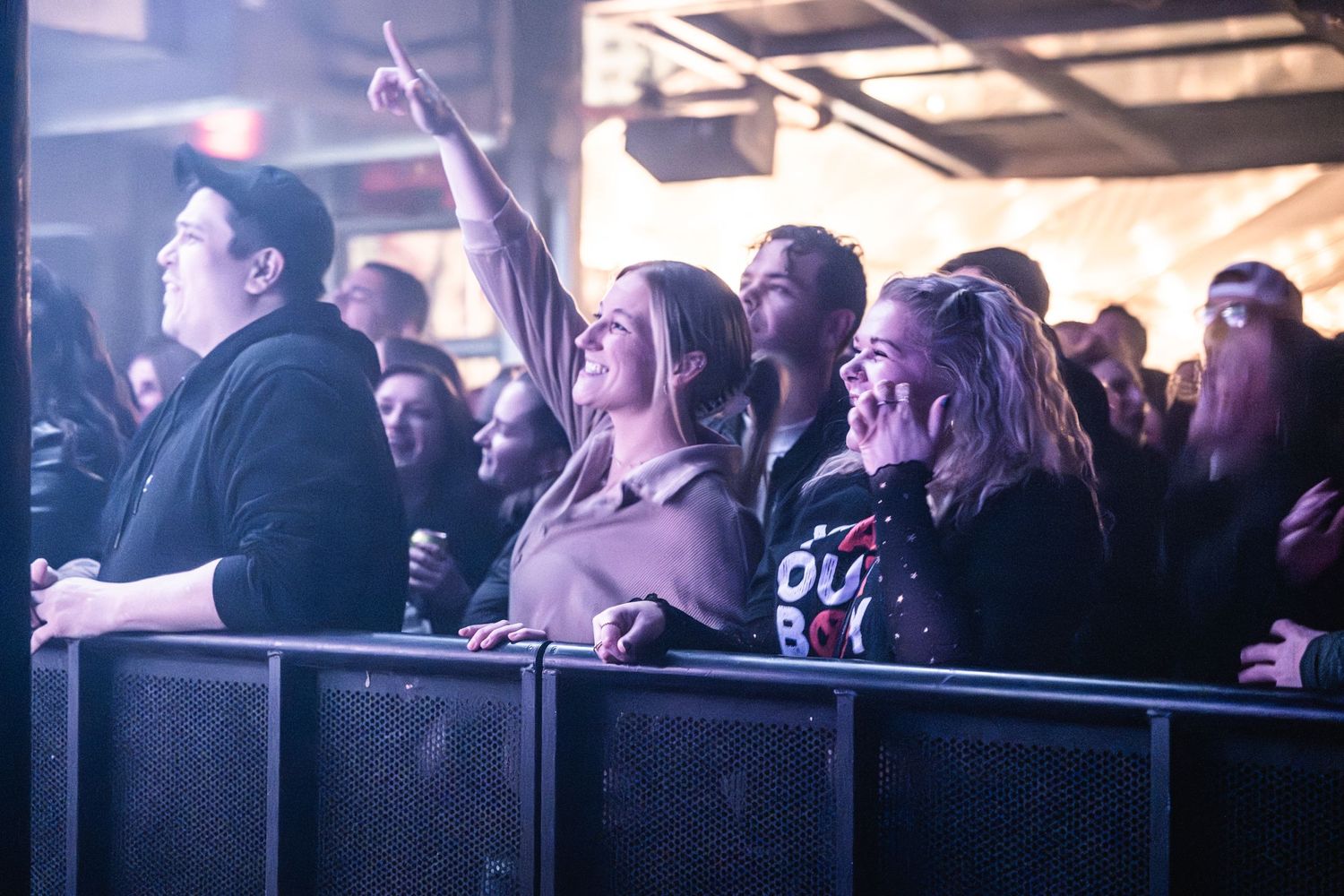 Concert crowd watching enthusiastically from behind barrier at live music show.