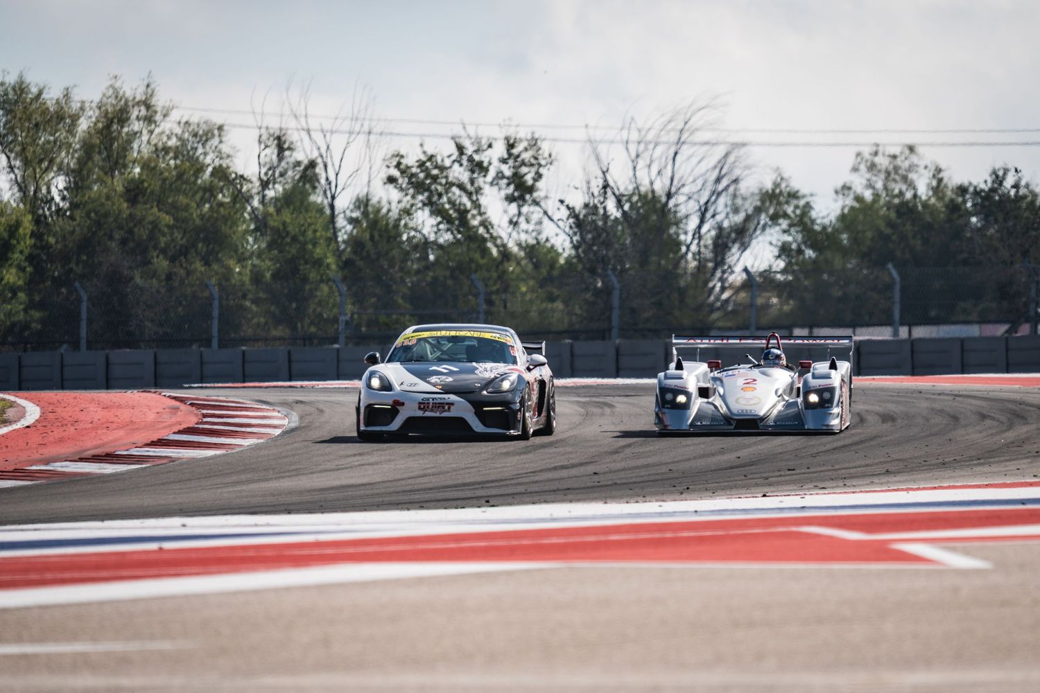 Two race cars compete through a tight corner on a professional motorsport circuit.