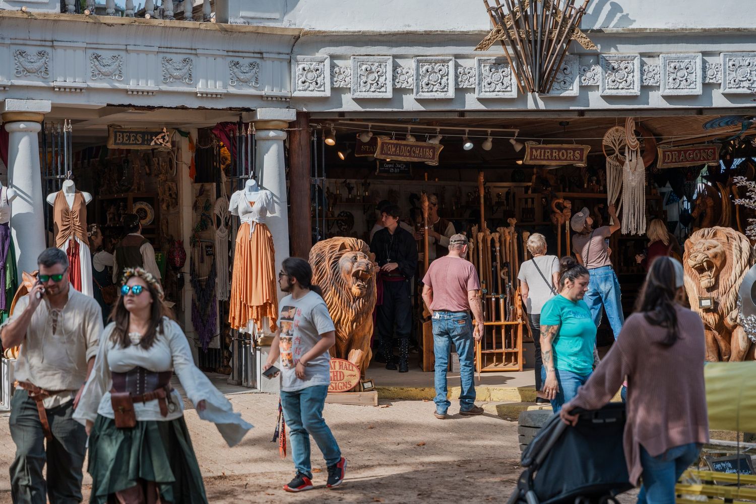 Medieval marketplace with clothing vendors and fairgoers browsing outdoor stalls at a renaissance festival.