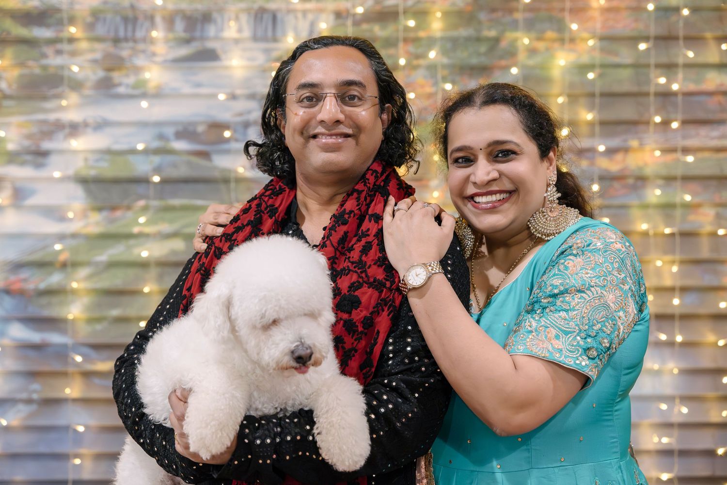 Two people holding a white fluffy puppy posing against a sparkly backdrop.