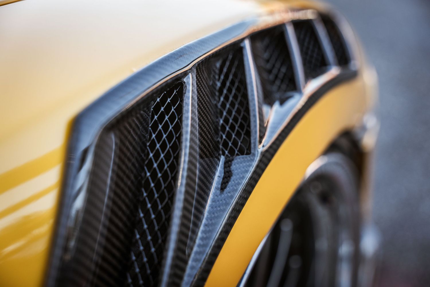 Close-up detail shot of a luxury vehicle's carbon fiber air vent and yellow body panel.