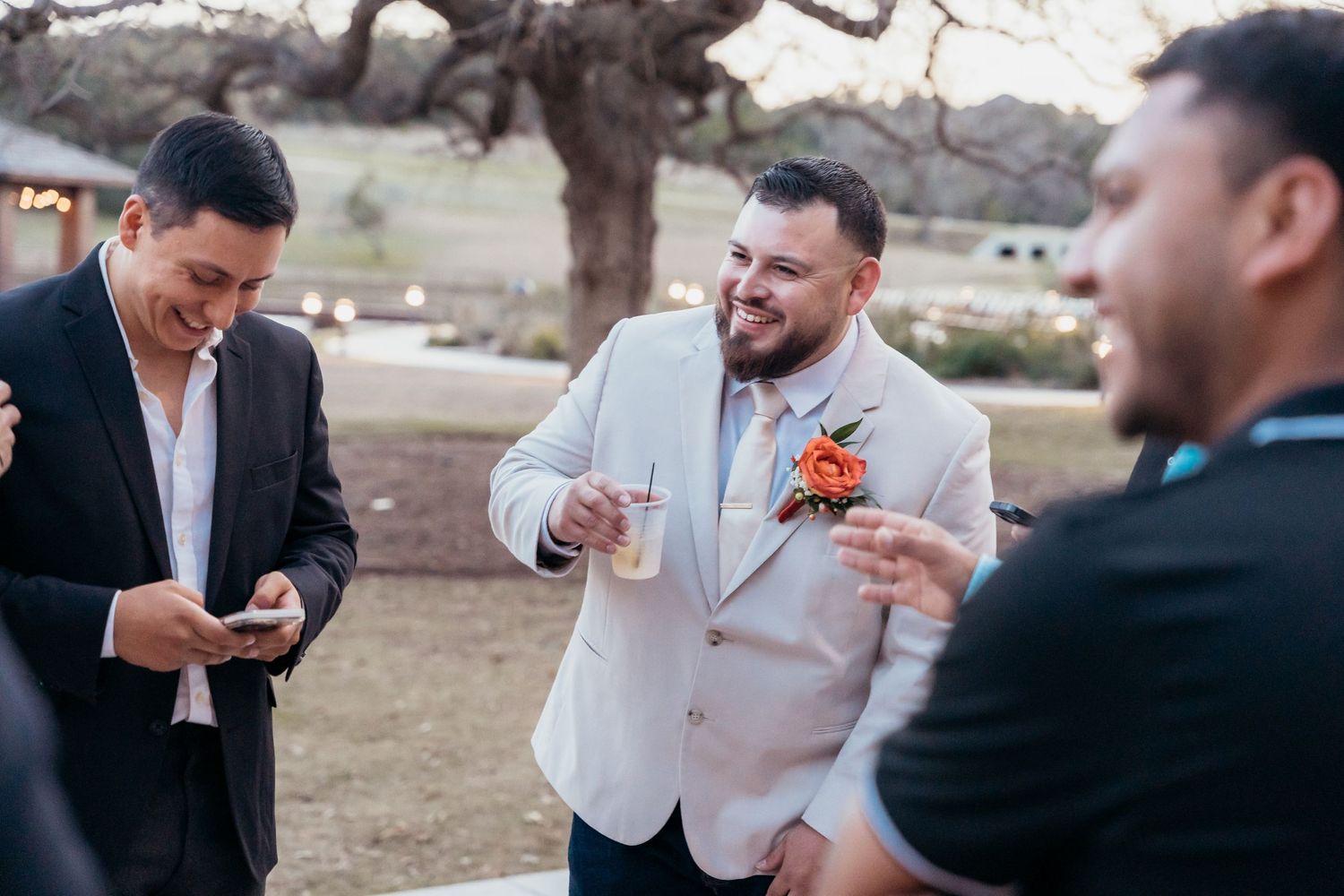 Wedding guests share drinks and laughter during an outdoor reception.