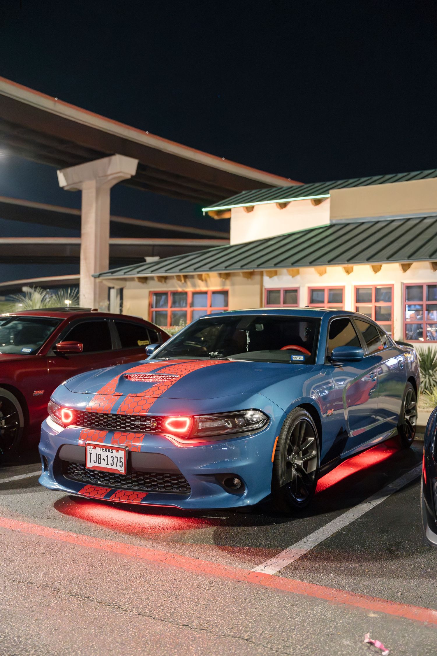 A modified blue Dodge Charger with red LED accents parked outside at night.