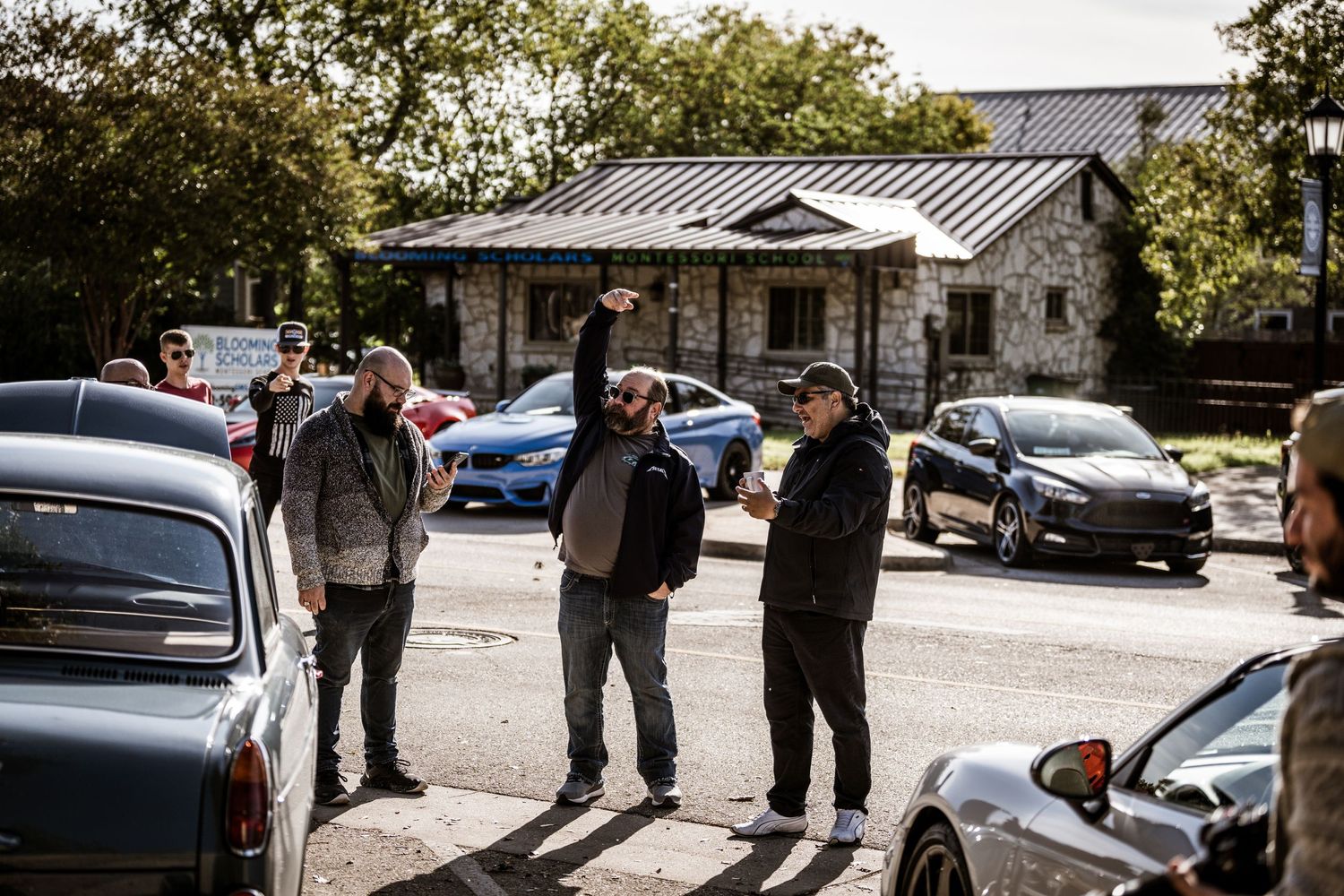 A group gathered in a parking lot during a car meetup event with various vehicles visible.