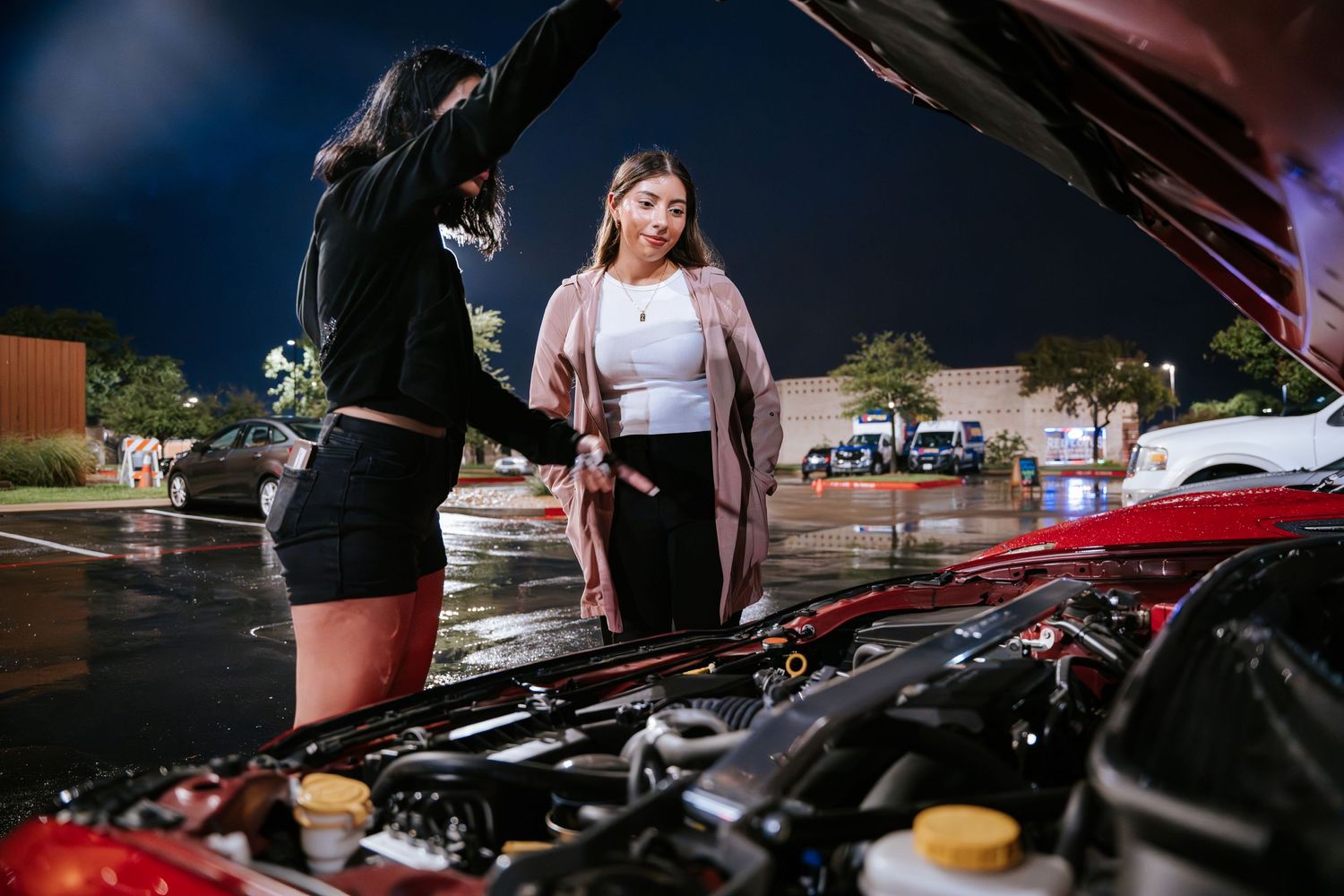 People examining the engine bay of a vehicle at a nighttime car meet.