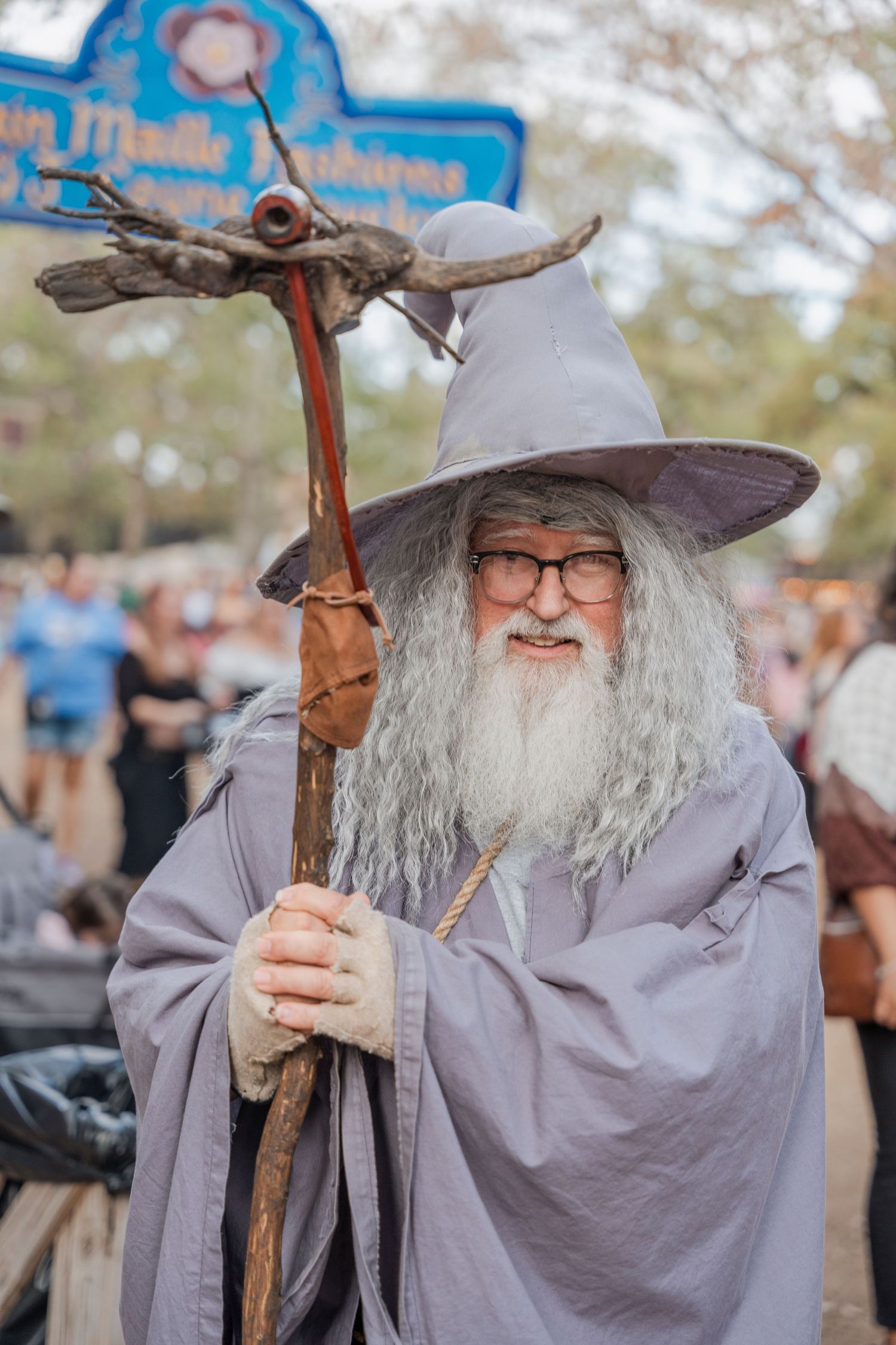 A costumed wizard character with gray robes and staff at a renaissance festival.