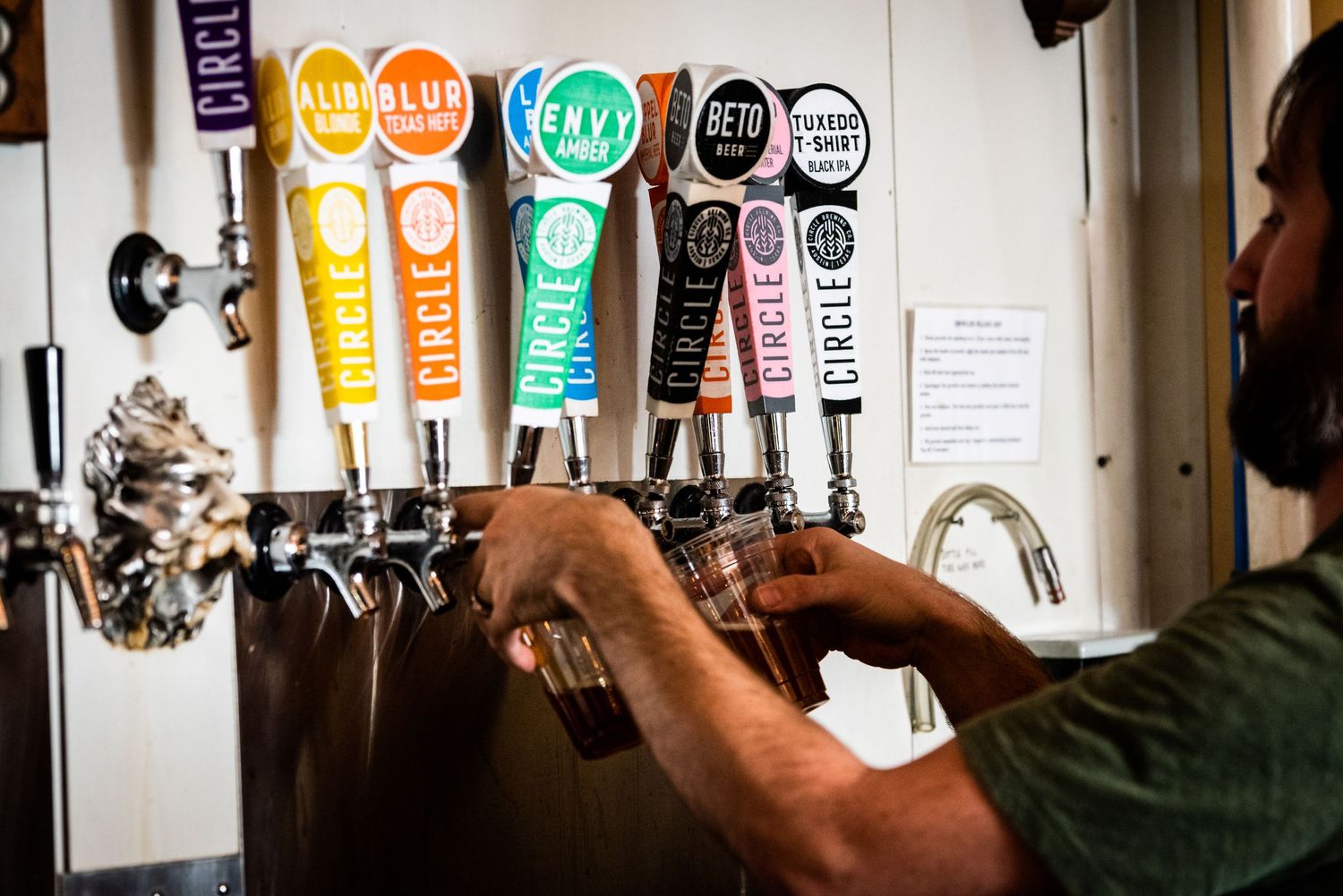 Row of colorful beer tap handles being operated at a bar counter.