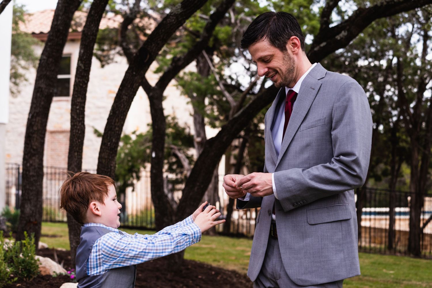 Sweet moment between man in grey suit and young boy in checkered shirt outdoors.