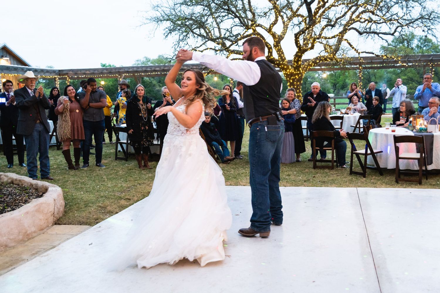 Couple dancing and twirling on a white dance floor at an outdoor rustic wedding venue.