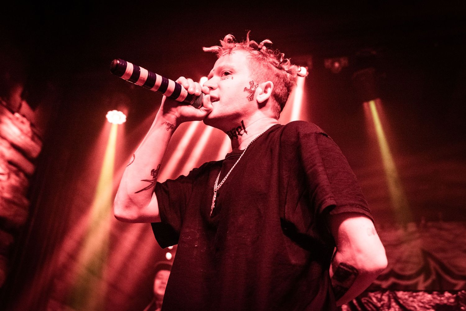 Concert performer in dark clothing singing under red stage lights.