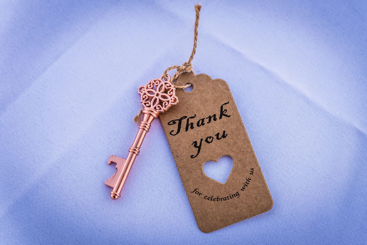 A vintage thank you tag with a decorative copper key attached by twine against a blue background.