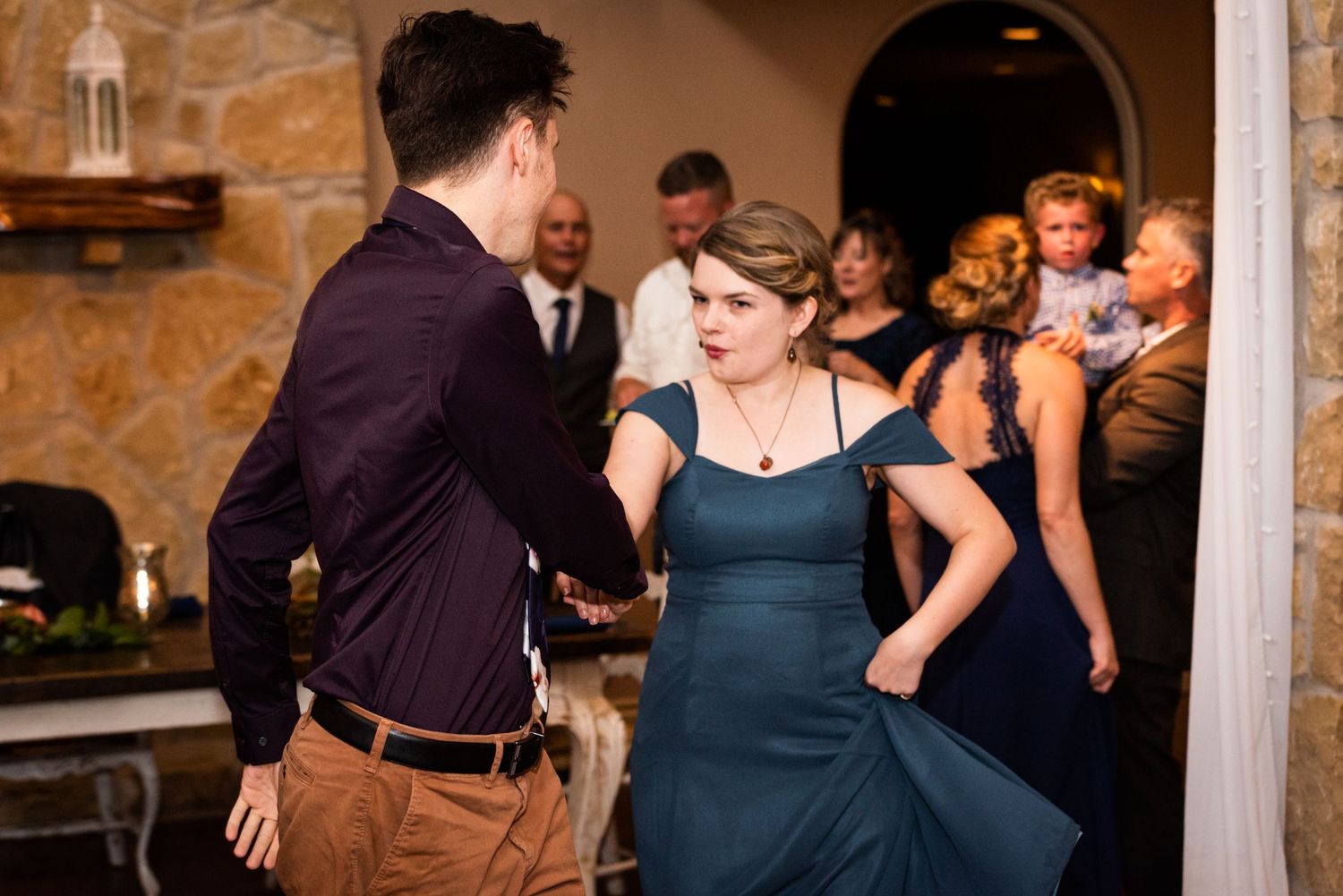 Reception guests dancing energetically at a rustic stone venue.