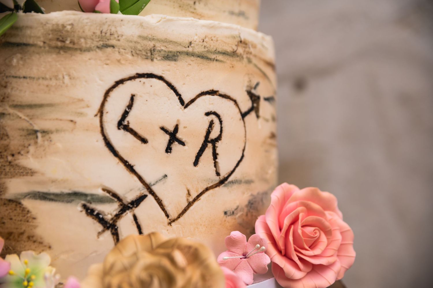 Heart with initials carved into birch bark with pink rose decoration.