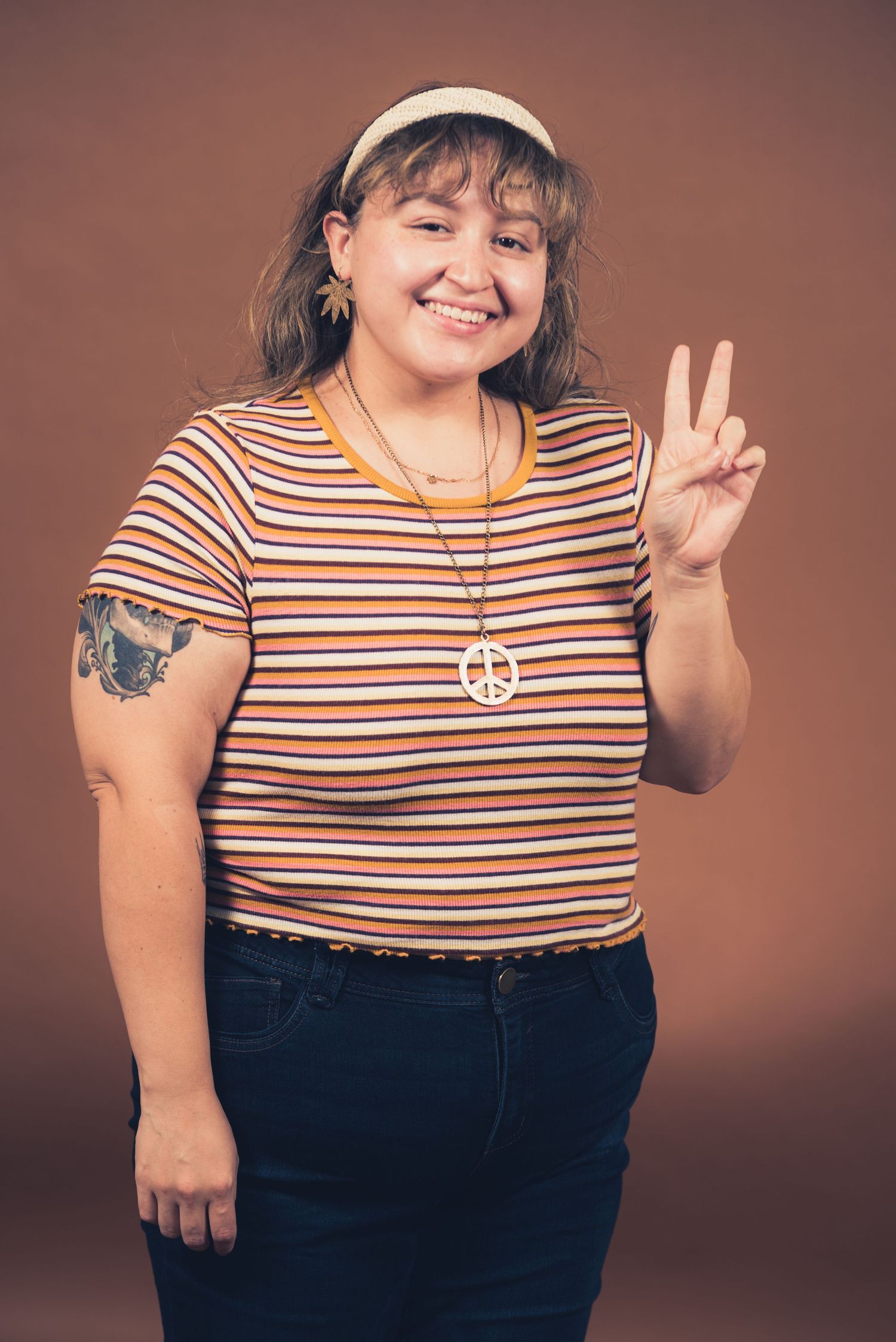 Person in striped shirt and headband making peace sign while smiling at camera.