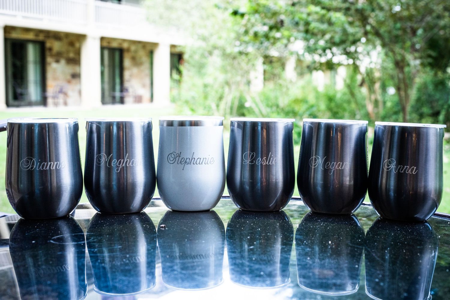 Row of black and white insulated wine tumblers displayed on reflective surface outdoors.