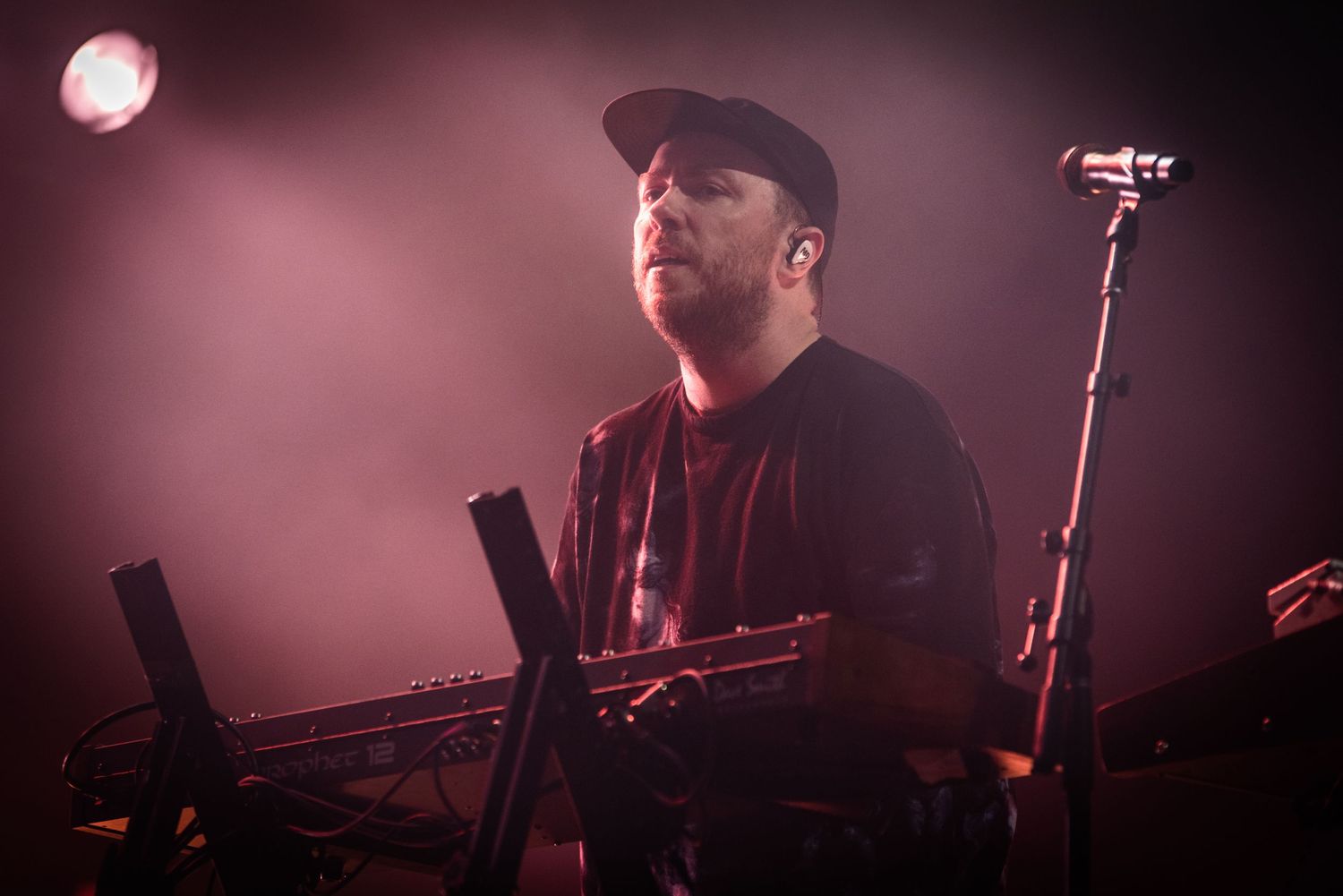 Concert performer illuminated by dramatic red lighting while operating electronic music equipment on stage.