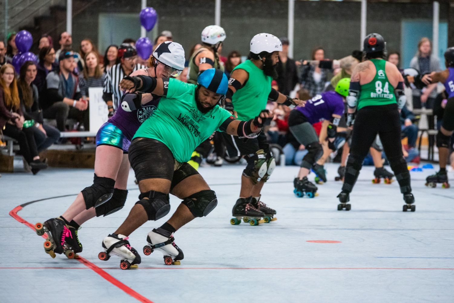 Roller derby players in green uniforms skate in formation during intense match.