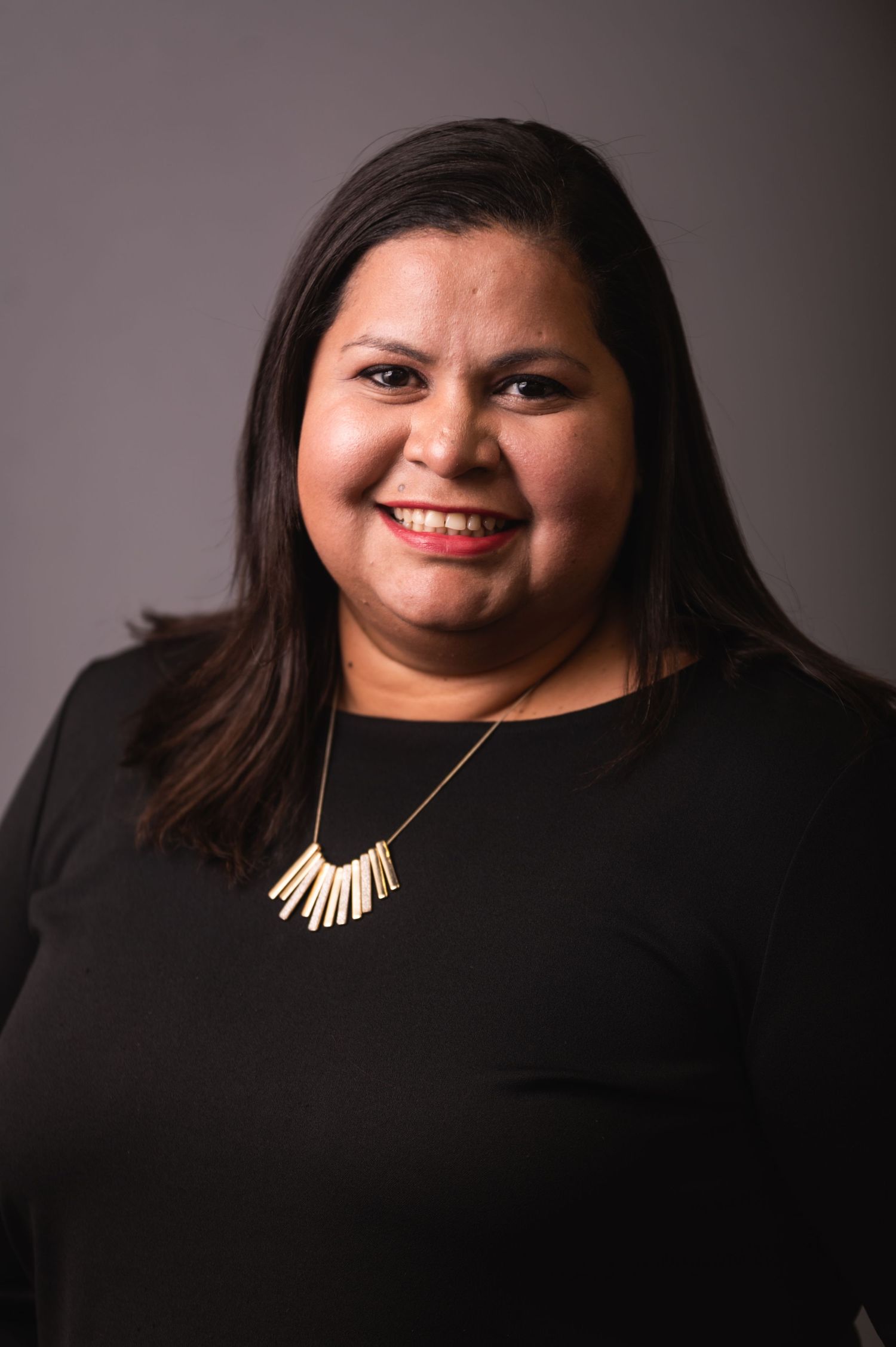 Studio portrait featuring black top and statement necklace against gray background.