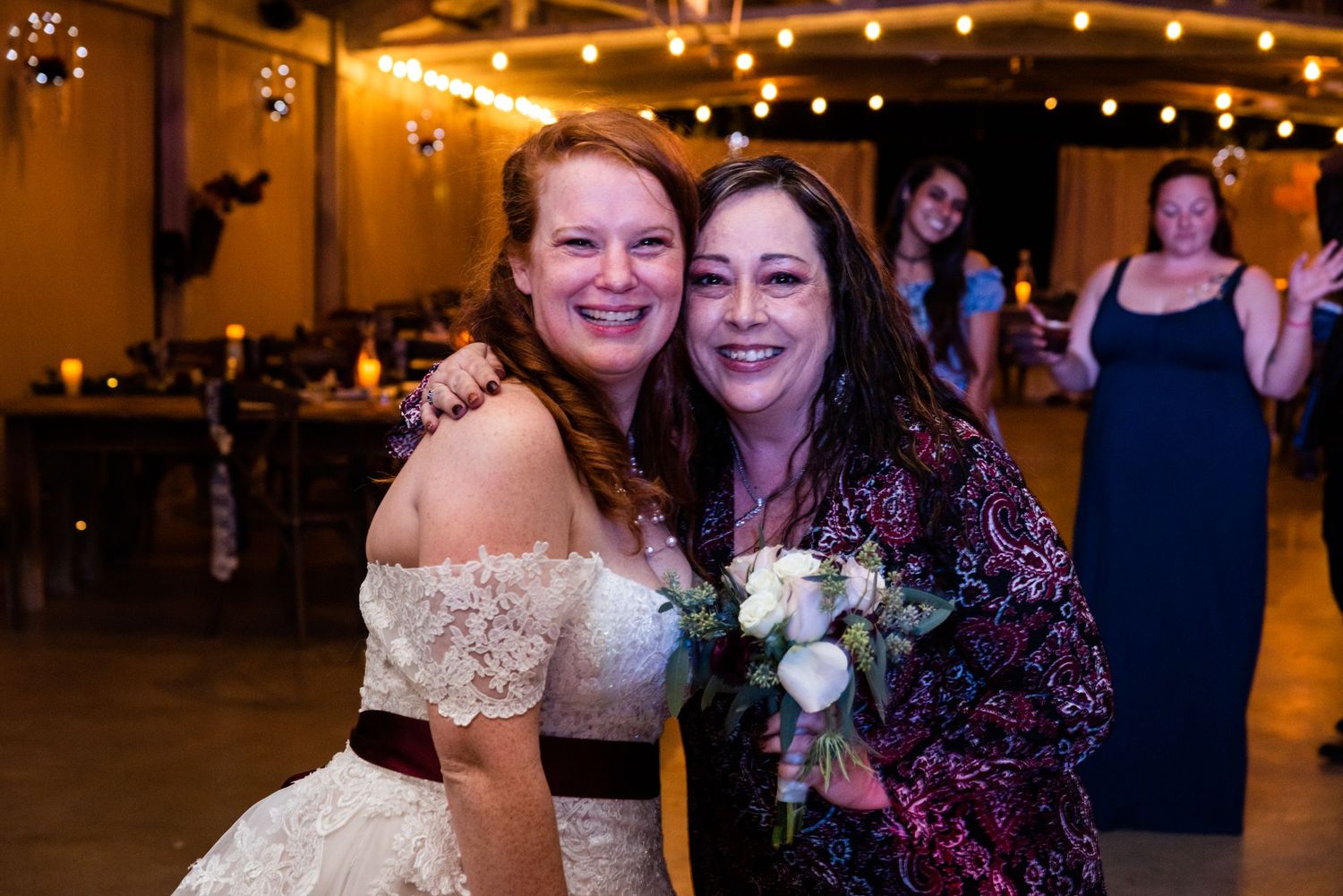 Wedding celebration with guests posing and smiling with bouquet in rustic venue.