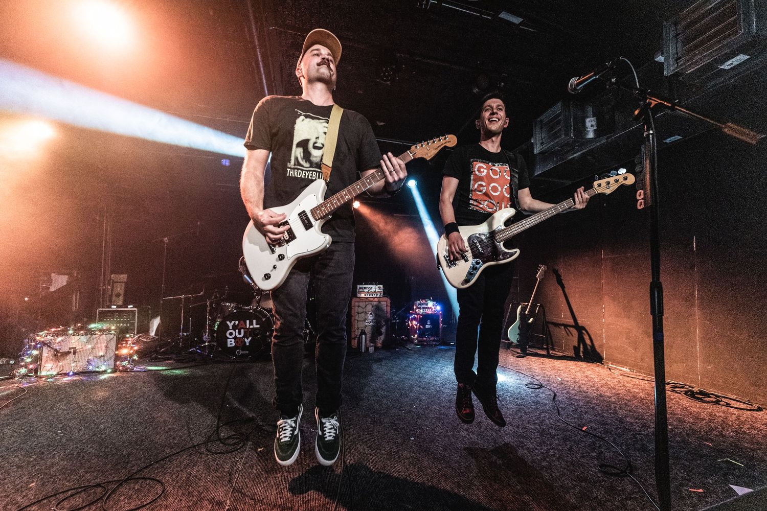 Rock band members performing with guitars on dimly lit concert stage.