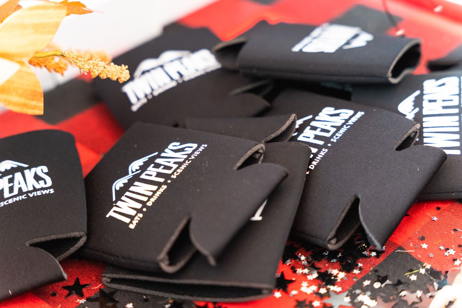 Stack of black drink koozies with white logo branding displayed on red surface.