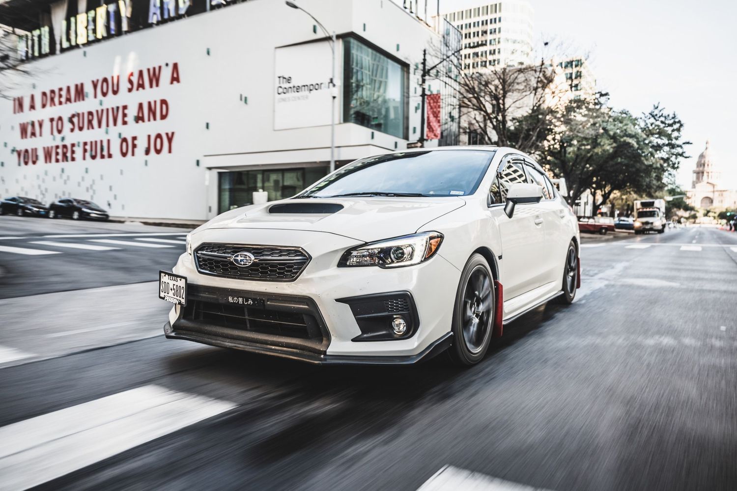 Modified white Subaru WRX STI photographed in motion against urban street art background.