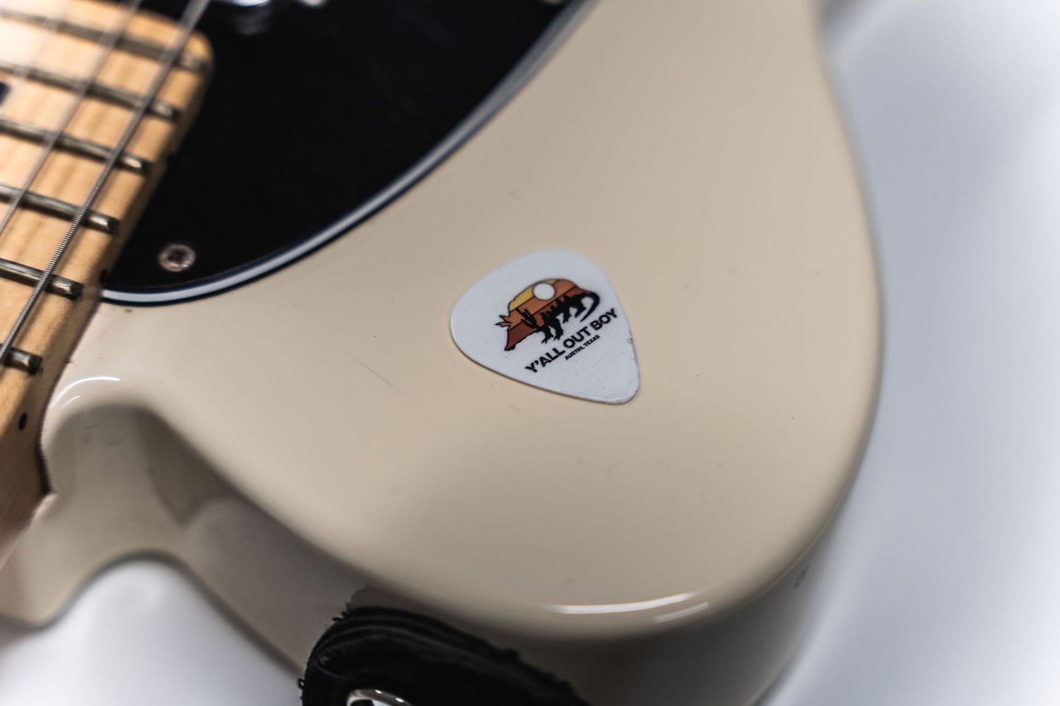 Close-up shot of a guitar pick on a cream-colored electric guitar surface.