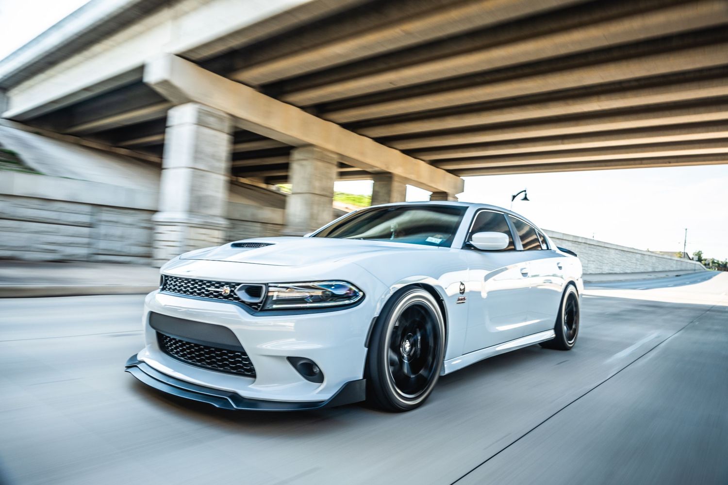 Low angle shot of white Dodge Charger driving under highway overpass.
