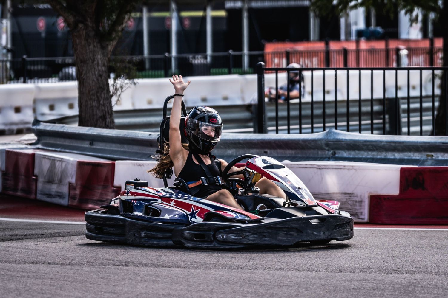 Go-kart racer navigating a tight turn on an outdoor karting circuit with red and white barriers.