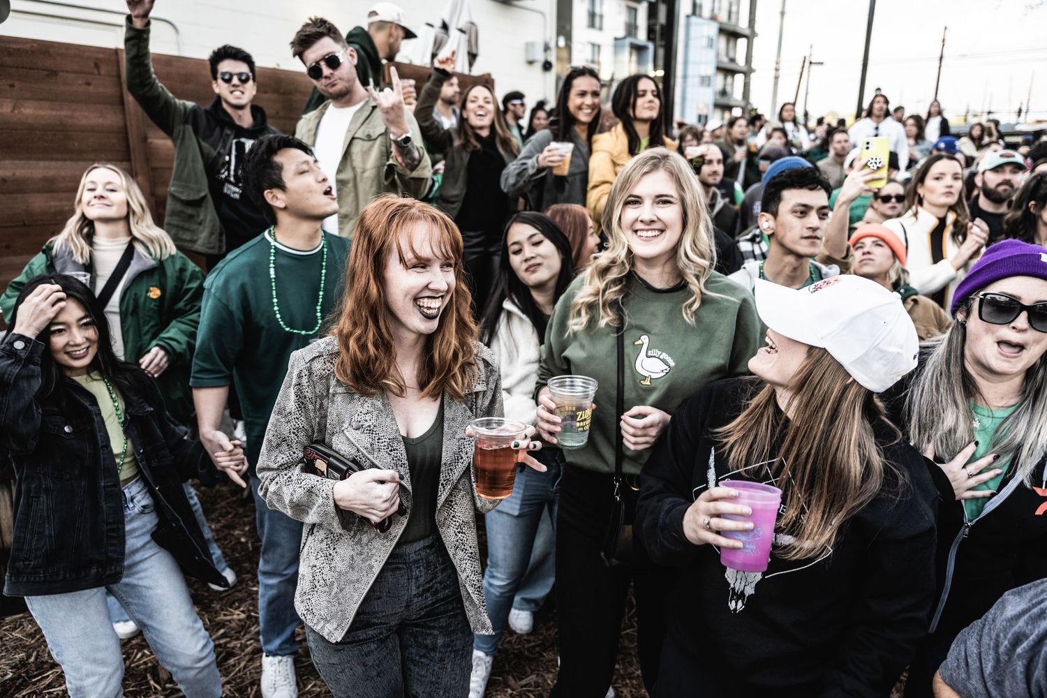 Festive crowd of young people holding purple cups at an outdoor celebration.