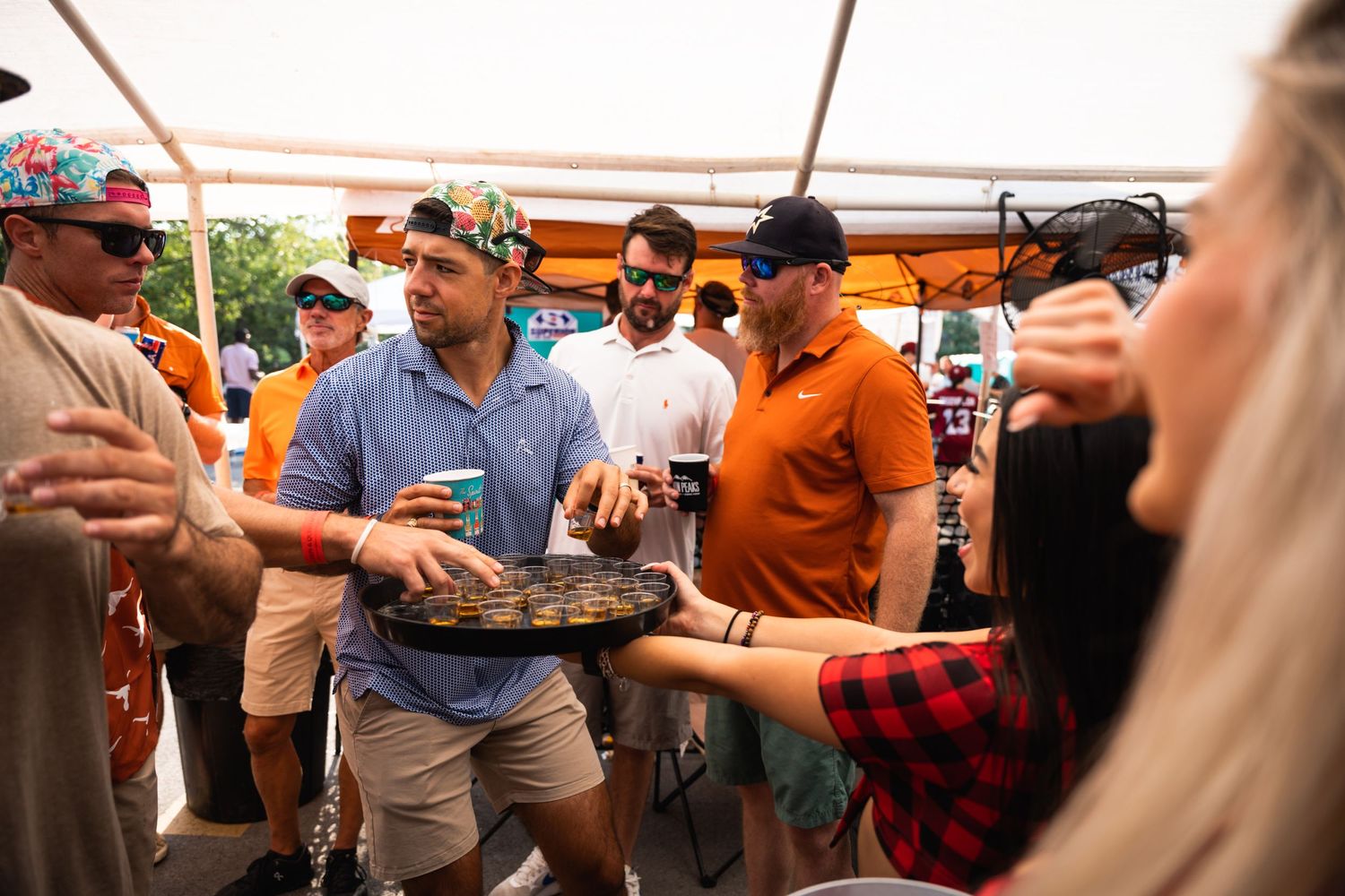 People gathered around sharing drinks and food at an outdoor tent party.