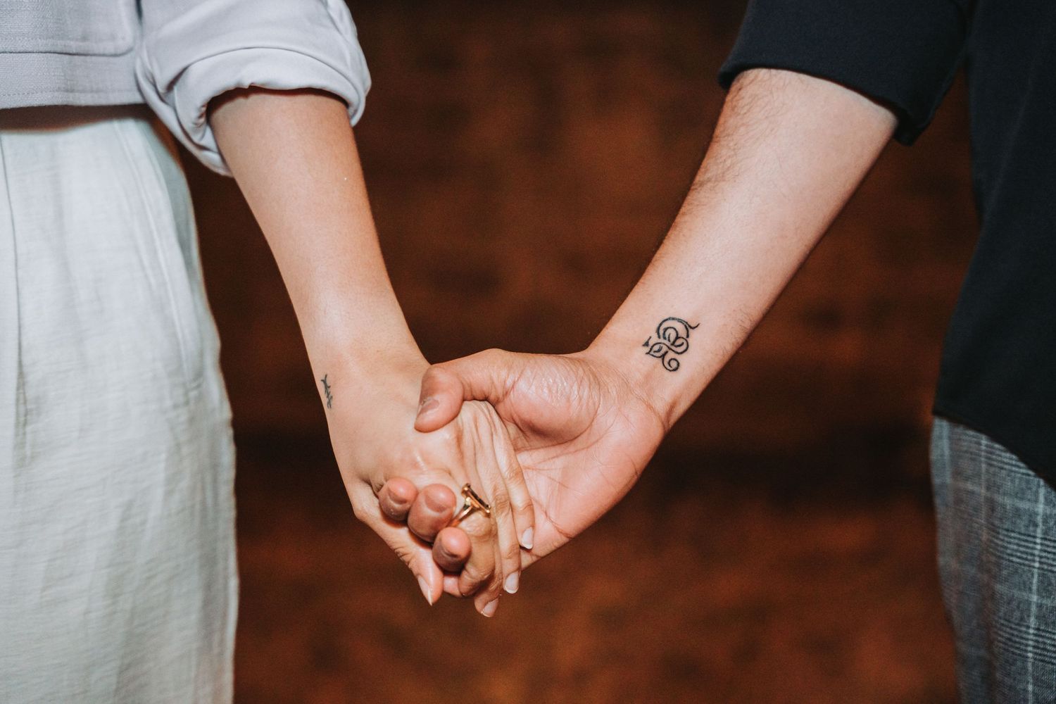 Close-up shot of two people holding hands with a small tattoo visible.